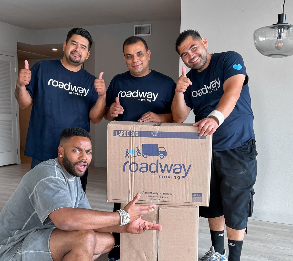 Roadway movers behind a cardboard box, with one of our customers posing in the front.