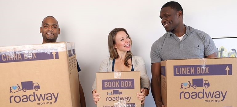 A group of people smiling and holding moving boxes.